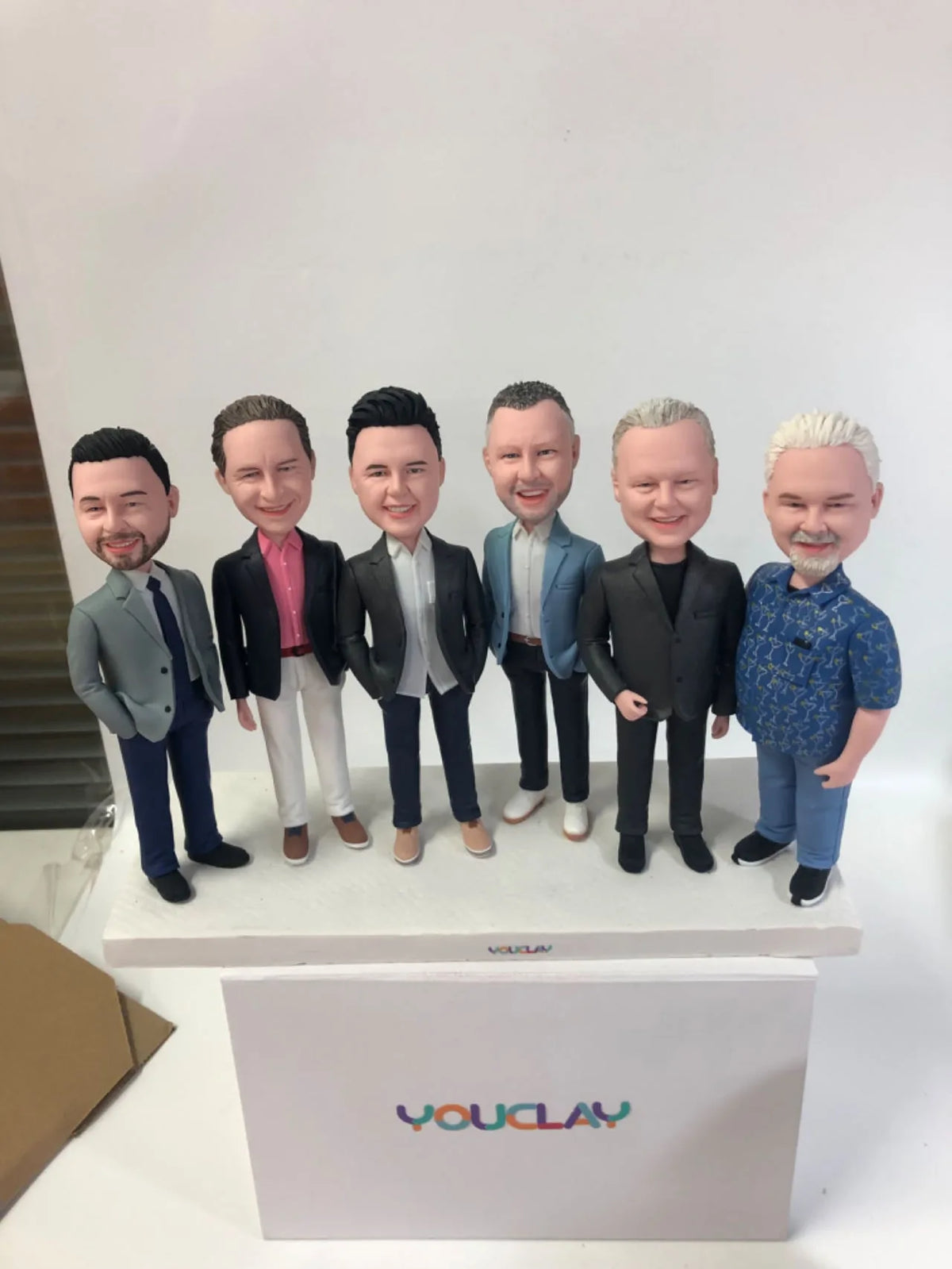 Six men in blazers and casual shirts standing in a row, a group of polymer clay figurines