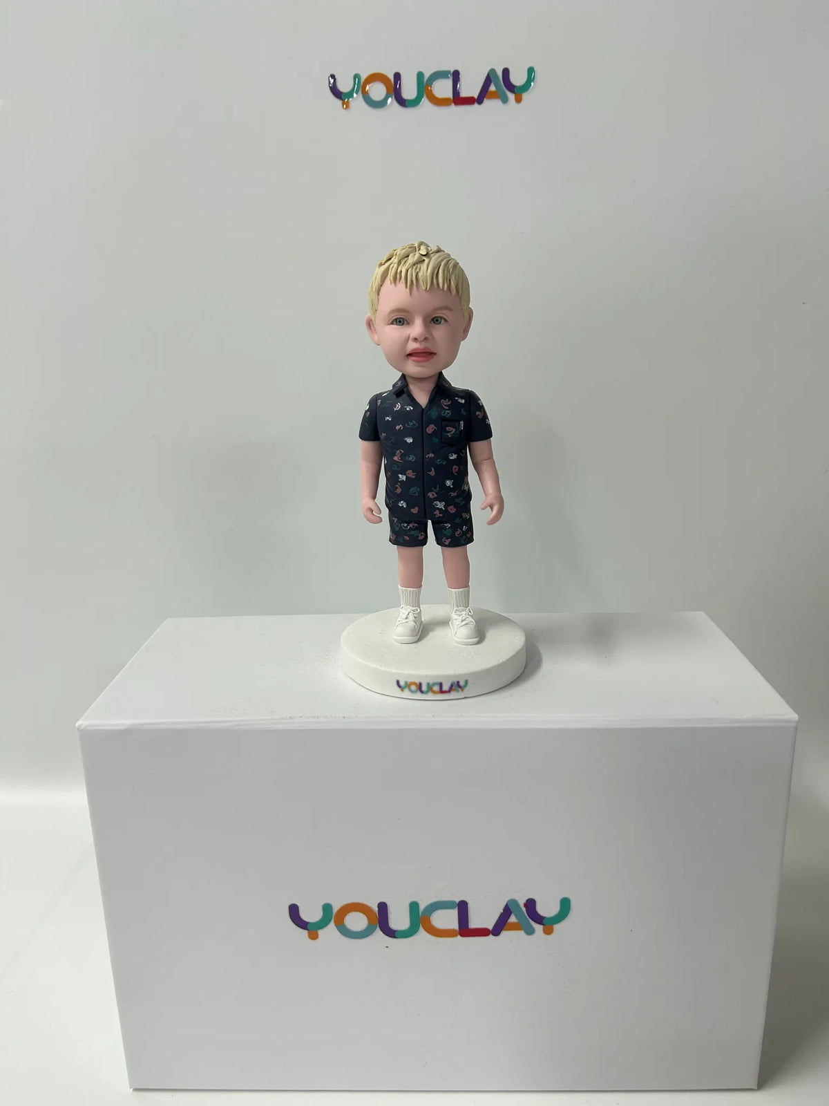 Blond toddler in a navy patterned shirt and shorts, white socks, as a handmade clay figurine