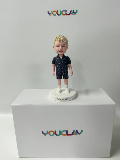 Blond toddler in a navy patterned shirt and shorts, white socks, as a handmade clay figurine