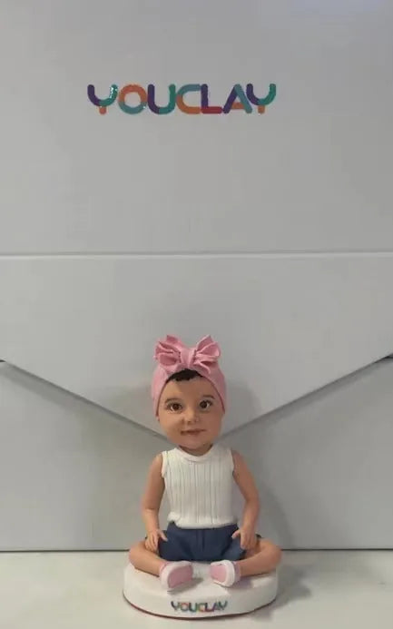 Seated baby girl in a big pink headband bow and white top, sculpted in polymer clay