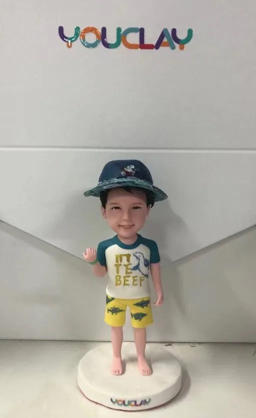 Little boy in a bucket hat, shark tee and yellow swim shorts, waving, as a custom bobblehead