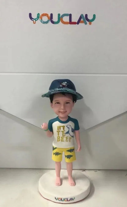 Little boy in a bucket hat, shark tee and yellow swim shorts, waving, as a custom bobblehead
