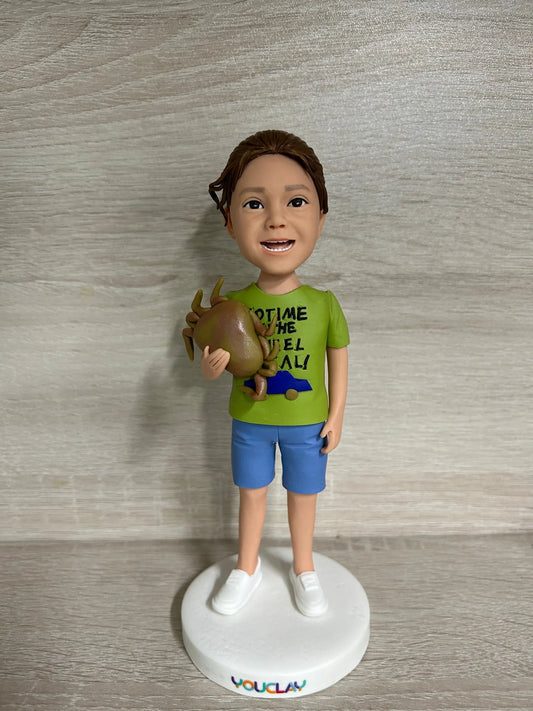 Smiling boy in a green graphic tee and blue shorts holding a toy, a custom child bobblehead on wood