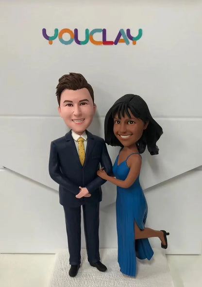 Polymer clay couple figurine: man in navy suit and gold tie, woman in a blue slit gown kicking one heel up