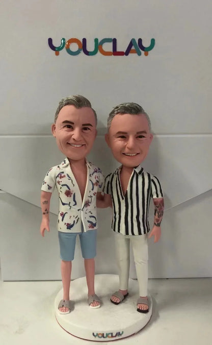 Two smiling men as custom bobbleheads in a floral shirt and a striped shirt, arm in arm on a round base