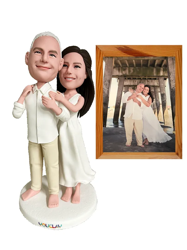 Barefoot beach wedding couple in white and cream, hugging, next to the framed pier photo used as reference