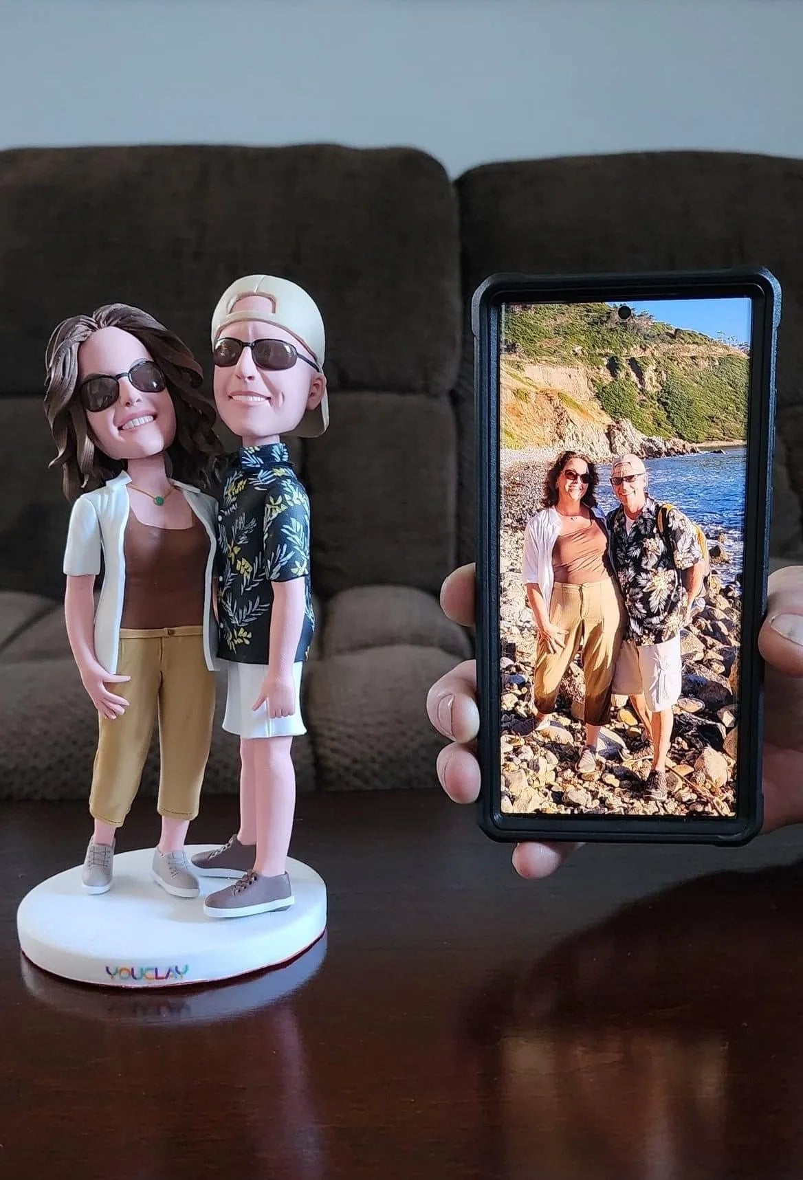 Couple in sunglasses sculpted from a seaside photo, the figurine held up next to the phone picture