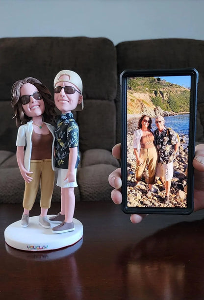 Couple in sunglasses sculpted from a seaside photo, the figurine held up next to the phone picture