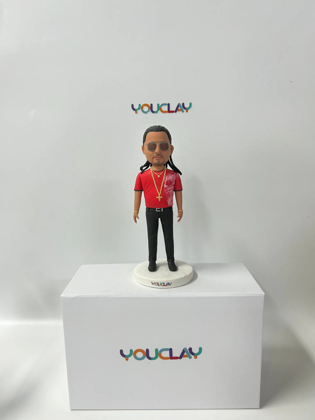 Polymer clay figurine of a man in a red T-shirt, aviator sunglasses and long braids, with a gold chain