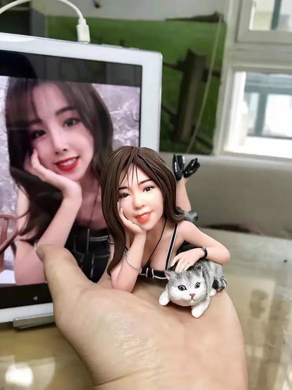 Clay figurine of a woman lying on her stomach with a gray kitten, held in a hand in front of her photo