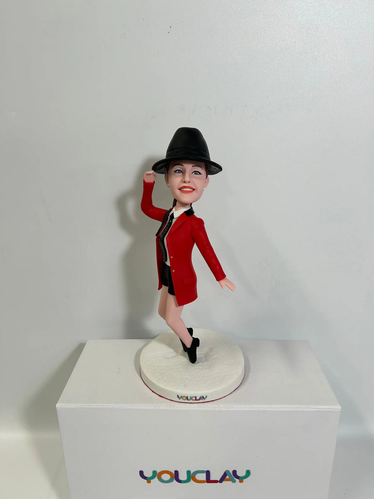 Custom bobblehead of a woman in a red ringmaster jacket and black fedora, posing on one leg on a white base