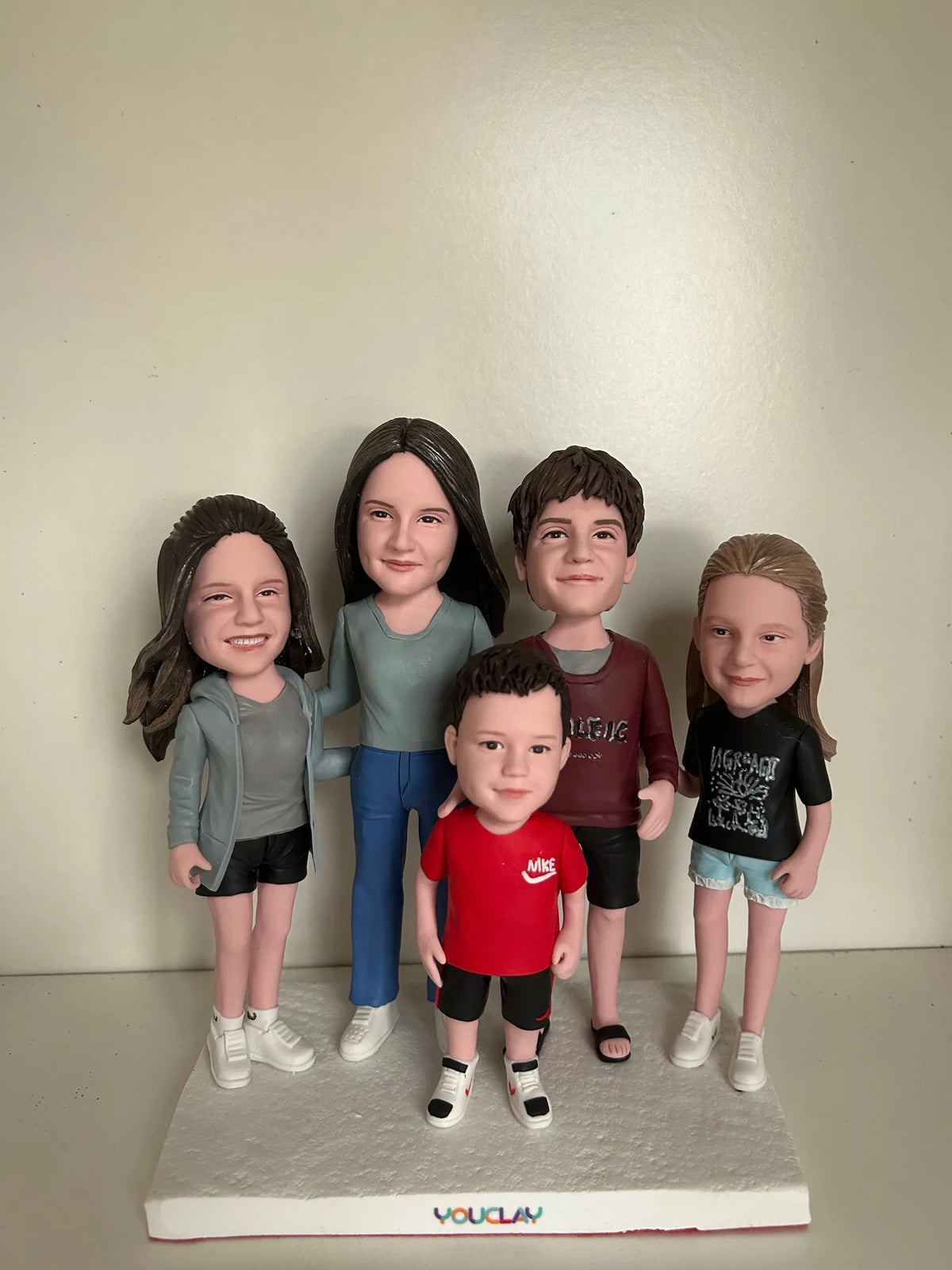 Five siblings and parents in casual clothes, a small boy in a red Nike tee in front, in polymer clay