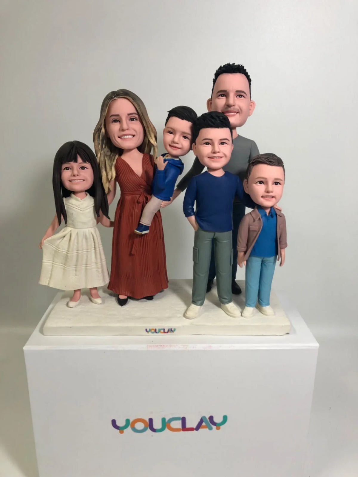 Six-person family with a girl in a white dress, mom in rust, and dad lifting a boy, in polymer clay