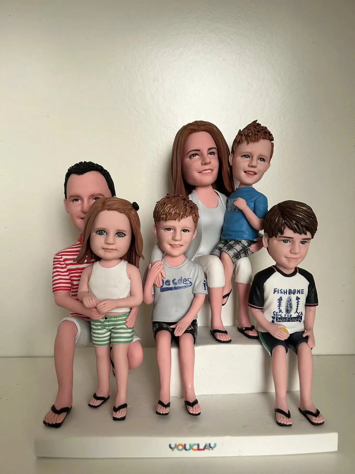 Dad, mom and four kids sitting on a white bench in summer clothes, set of 6 clay figurines