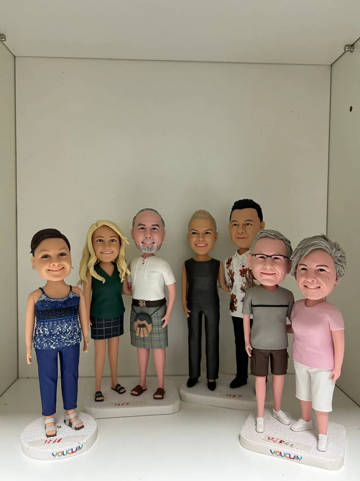 Seven figurines on three bases including a man in a kilt and a couple in pink and gray