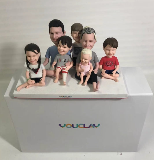 Seven family members sitting together with a baby and kids in front, a cozy custom bobblehead set