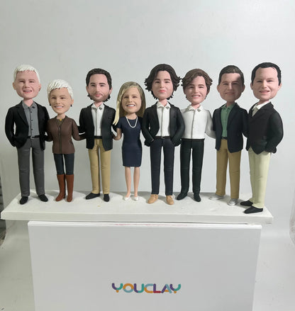 Eight adults in blazers, jeans and a navy dress lined up in a row, hand-sculpted in polymer clay
