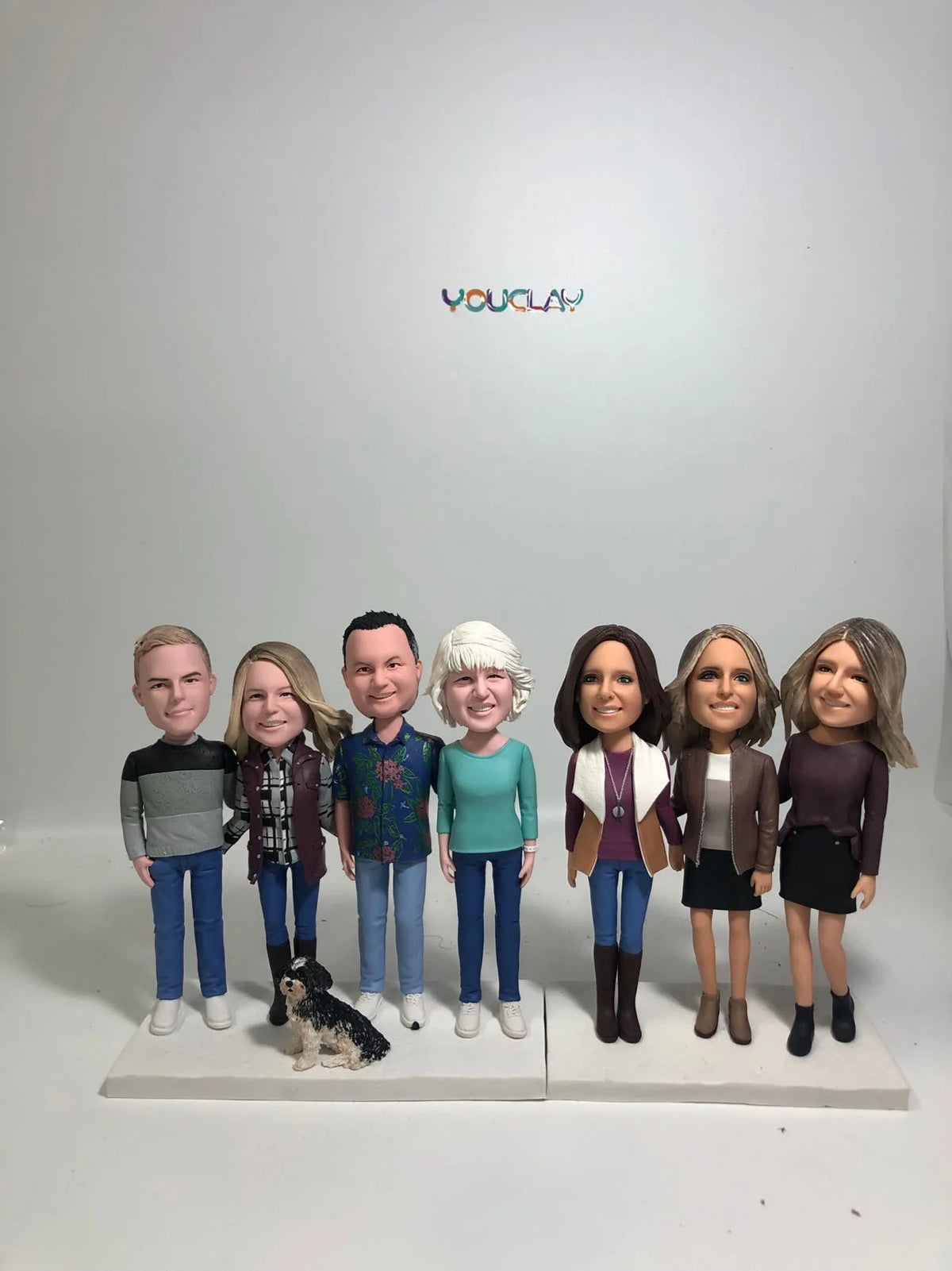 Seven adults in casual fall clothes with a small black and white dog, a family of custom bobbleheads
