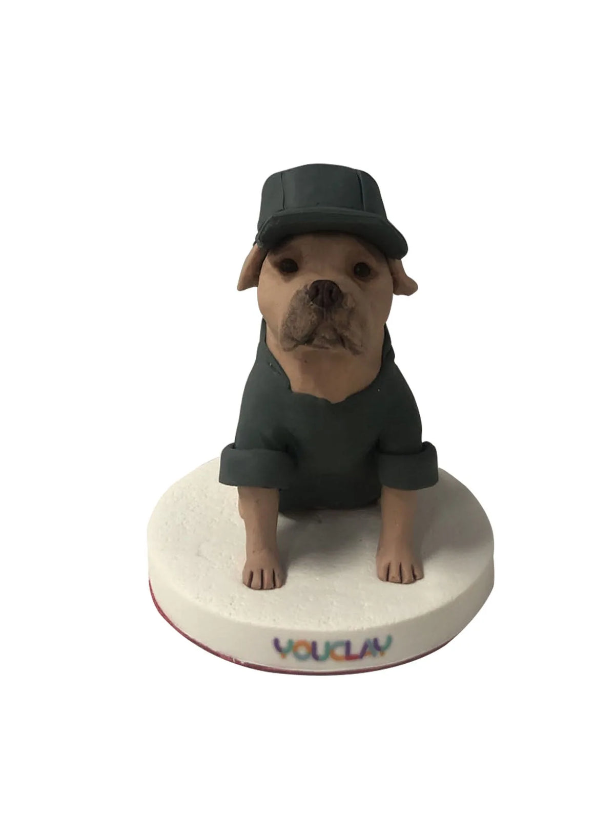 Tan pit bull wearing a black cap and shirt, sitting upright, a handmade clay dog figurine